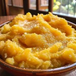 Purê de batata-doce cremoso em uma tigela branca, com uma colher ao lado.