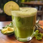 Close-up de um copo de Suco Detox de Abacaxi e Hortelã, com ingredientes frescos ao fundo.