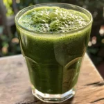 Smoothie Verde Detox em um copo, com ingredientes frescos ao fundo.