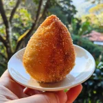 Close up of a golden-brown Coxinha filled with shredded chicken.