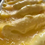 Uma mousse de maracujá cremosa em um recipiente de vidro, vista lateral, com textura suave e cremosa.