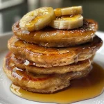 Panquecas de banana fofinhas empilhadas em um prato, com fatias de banana por cima.