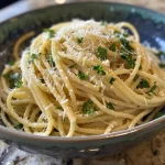 Prato de massa com limão, alho e queijo parmesão, servido em uma tigela branca.