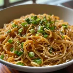 Prato com macarrão frio de gergelim, molho cremoso e sementes de gergelim por cima.