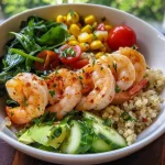 Close-up of a quinoa bowl with shrimp, colorful vegetables, and herbs.