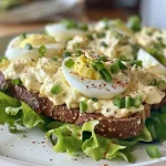 Salada de ovo cremosa em uma fatia de pão, vista lateral.