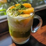 Close-up de um Iced Peach Matcha Latte com uma fatia de pêssego ao lado.