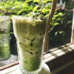 Latte de matcha gelado em um copo transparente com camadas visíveis.