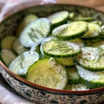 Salada de pepino com iogurte e dill em close, com ingredientes frescos ao fundo.