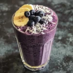 Close-up view of a creamy banana blueberry smoothie in a glass with blueberries on top.