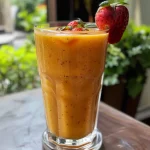 Smoothie de morango e manga com frutas frescas ao fundo.