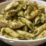['Close-up de massa de frango com pesto.', 'Prato de penne com pedaços de frango e molho pesto.', 'Chicken pesto pasta servida com creme de leite.', 'Massa com frango e molho pesto em ângulo lateral.']