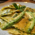 ['Ravioli de abacate recheados, com a massa fina e bem apresentada.', 'Close-up de um ravioli de abacate, mostrando sua textura e recheio.', 'Ravioli de abacate com detalhes de ervas e azeite, em destaque.', 'Porção de ravioli de abacate, evidenciando o acabamento e os ingredientes.']
