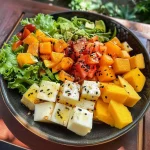 ['Salada tropical colorida com manga, abacaxi e folhas verdes.', 'Close de uma salada tropical com ingredientes frescos e vibrantes.', 'Salada tropical com cubos de manga, abacaxi e pimentão vermelho.', 'Prato de salada tropical com nozes e coco ralado em cima.']