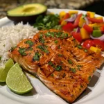 ['Filé de salmão grelhado com salsa de manga e arroz de coco.', 'Salmão suculento acompanhado de salsa fresca e arroz de coco cremoso.', 'Prato de salmão grelhado com guarnição de manga e arroz de coco.', 'Salmão grelhado servido com salsa de manga e arroz de coco.']