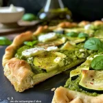['Close-up de uma torta salata de pesto e abobrinha, mostrando a textura suculenta.', 'Vista lateral da torta salata com pesto e abobrinha, ressaltando sua crocância.', 'Imagem detalhada de uma torta salata de pesto e zucchine, com camadas visíveis.', 'Torta salata de pesto e abobrinha, apresentando cores vibrantes e frescas.']