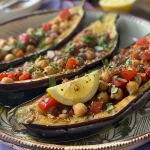 ['Berinjela assada com grão de bico e tahine.', 'Prato de berinjela mediterrânea com especiarias e leguminosas.', 'Close de berinjela com molho de tahine e grão de bico.', 'Berinjela assada servida com grão de bico e decorada com legumes.']