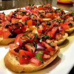 ['Bruschetta com tomates e manjericão sobre pão torrado.', 'Close-up de bruschetta fresca com ingredientes coloridos.', 'Fatias de bruschetta apresentando tomates e ervas frescas.', 'Pão baguete tostado coberto com bruschetta vibrante.']