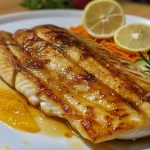 ['Filé de peixe dourado coberto com molho de maracujá.', 'Prato de filé de peixe com molho de maracujá em close.', 'Delicioso filé de peixe servido com molho de maracujá.', 'Filé de peixe com aparência suculenta e molho de maracujá.']