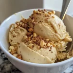 ['Gelado proteico cremoso em uma tigela com pepitas de chocolate.', 'Close-up de gelado cremoso proteico com textura suave.', 'Gelado cremoso proteico servido com bolachas sem açúcar ao lado.', 'Delicioso gelado proteico em uma colher, com fundo desfocado.']