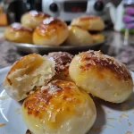 ['Pão de queijo recheado com frango, com textura crocante.', 'Close-up de um pão de queijo com frango desfiado no interior.', 'Pão de queijo cremoso exposto, mostrando o recheio de frango.', 'Pão de queijo com queijo e frango, visto de lado.']