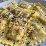 ['Ravioli de abóbora cremoso com molho branco.', 'Close de ravioli recheado de abóbora servido em prato elegante.', 'Prato de ravioli de abóbora cremoso coberto com queijo parmesão.', 'Ravioli de abóbora com molho rico e ingredientes frescos.']