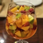 ['Copo de Sangria com espumante e frutas coloridas.', 'Bebida refrescante de Sangria com espumante e gelo.', 'Sangria servida em um copo com frutas picadas e espumante.', 'Close-up de uma taça de Sangria espumante com gelo.']