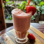 ['Smoothie cremoso de morango em um copo transparente.', 'Close-up de um smoothie de morango com textura cremosa.', 'Bebida saudável de morango em destaque, com iogurte e leite de coco.', 'Smoothie de morango servido em um copo, com cores vibrantes.']