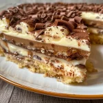 ['Fatia de Torta Holandesa com camada de chocolate.', 'Close-up de Torta Holandesa com recheio cremoso.', 'Lado da Torta Holandesa exibindo suas camadas.', 'Porção generosa de Torta Holandesa com chocolate branco.']