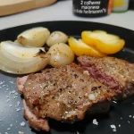 Carne assada ao molho de cebolas, com cebolas douradas ao fundo.